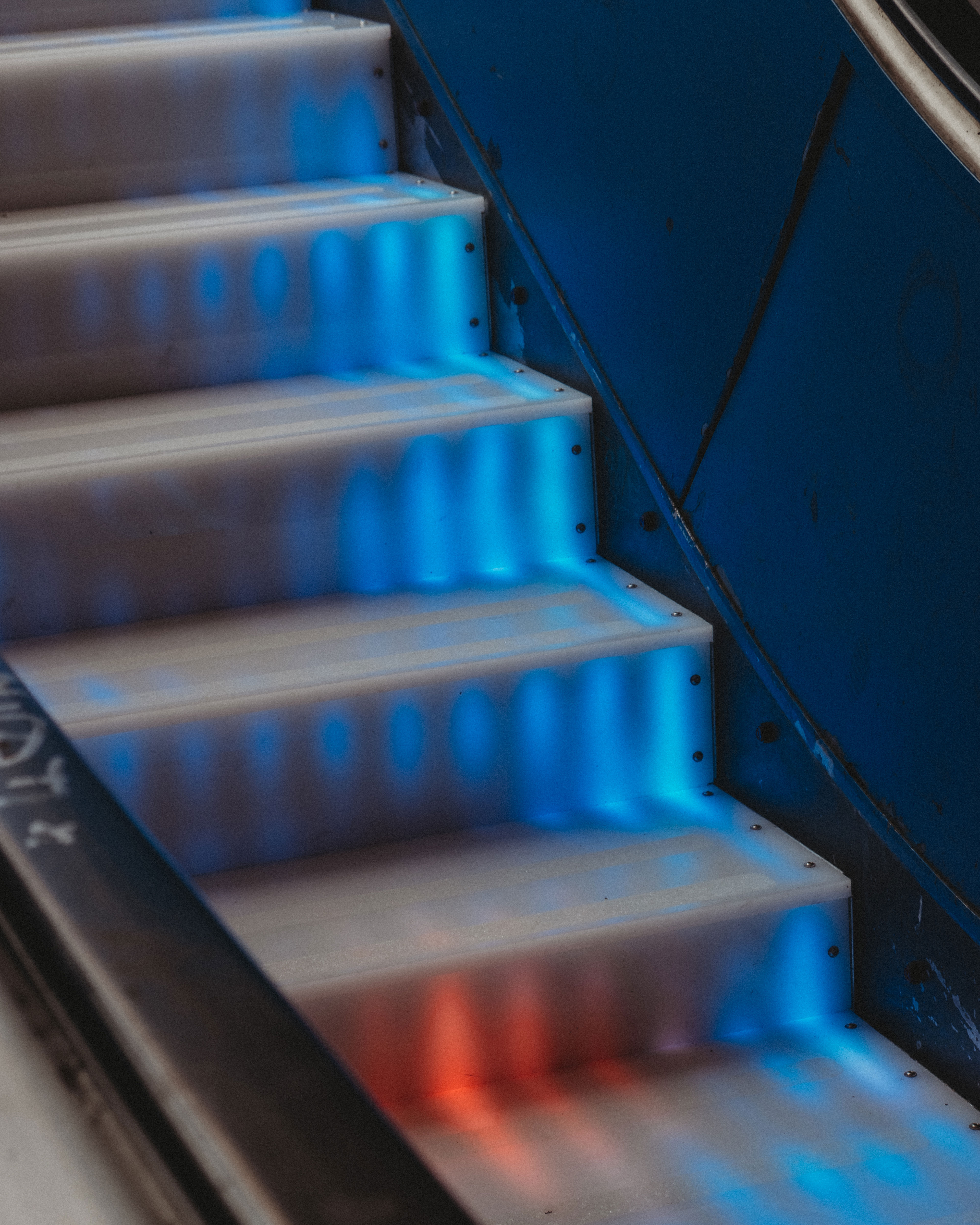Image of a set of stairs with blue and red lights illuminating each step. The lights create a dynamic pattern that moves as you look down the stairs.